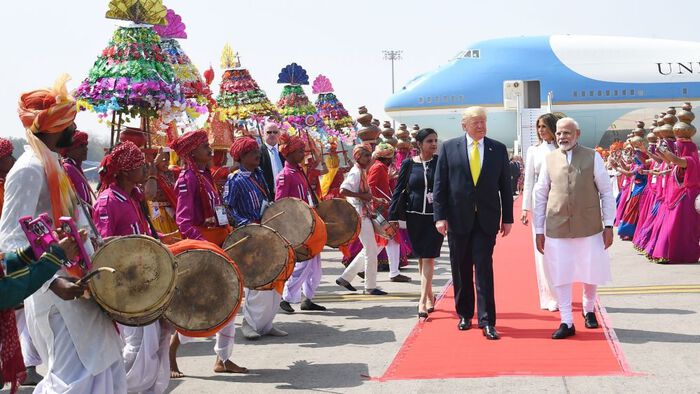 To menn p? en l?per p? foran et fly i India - to kvinner bak  Det er trump og Modi i front. Og masse indere med trommer og fargerike kl?r som tar imot dem. 